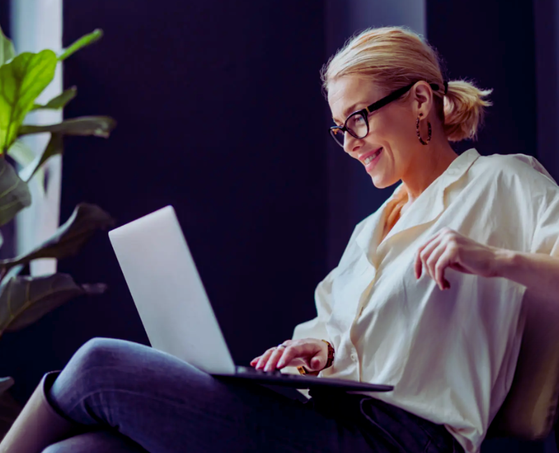 o femeie blonda imbracata office cu laptopul in poala, cu un aer lejer dar profi